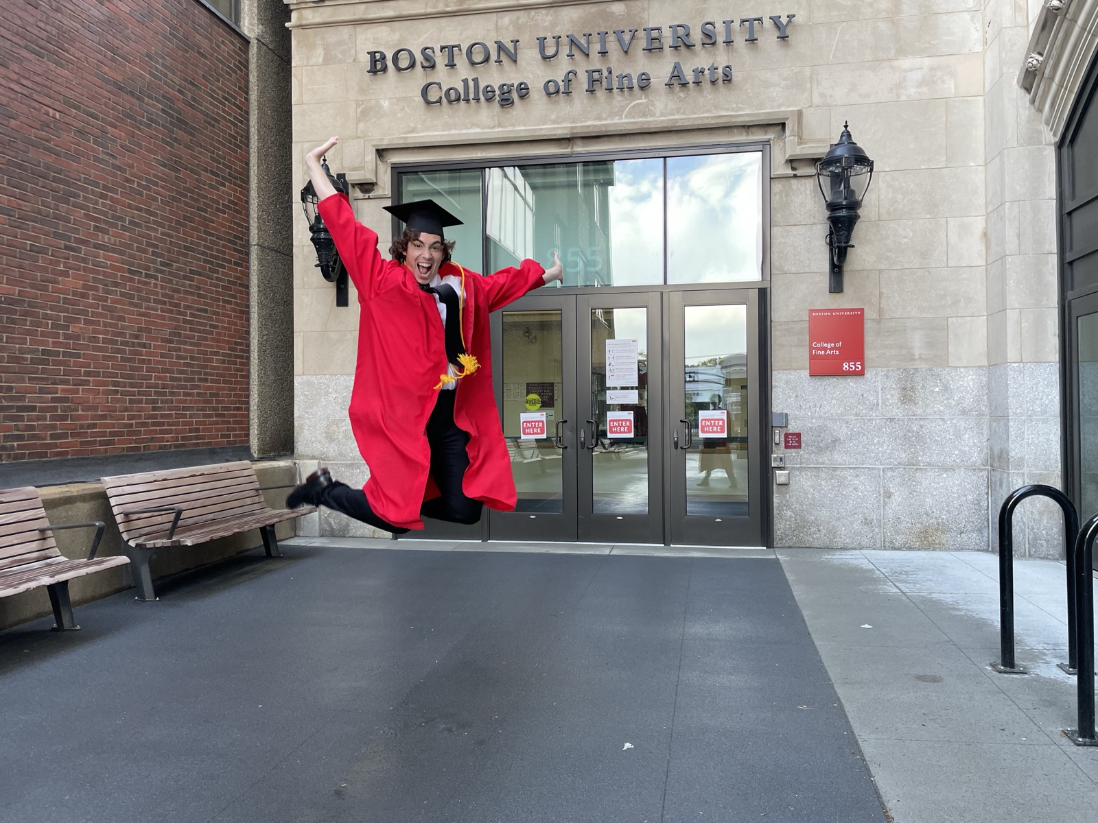 Neil Kelly leaping in cap and gown outside the Boston University College of Fine Arts