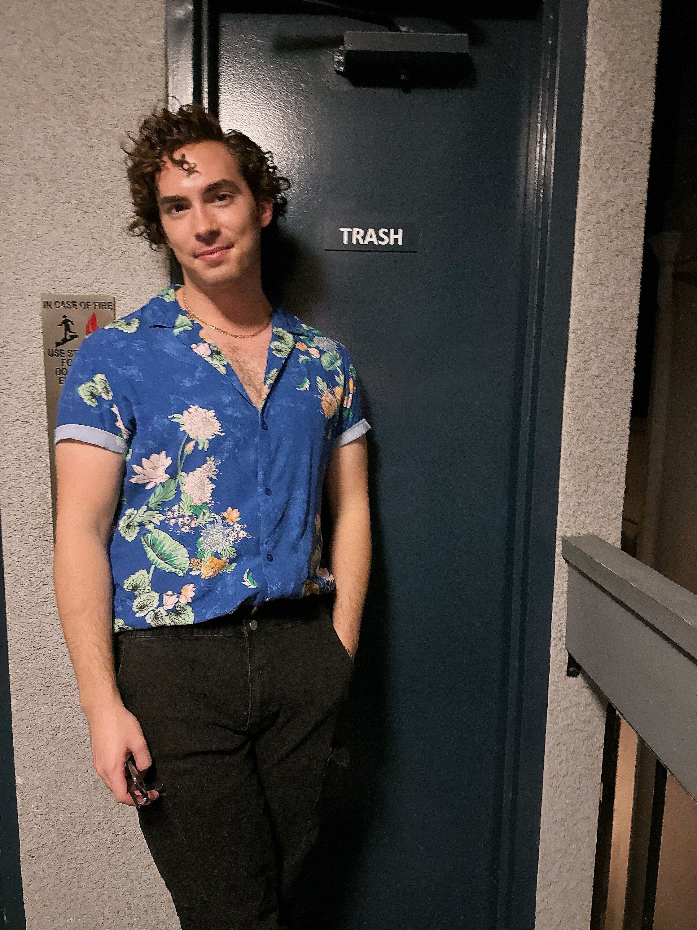 Neil in a blue floral shirt leaning against an exterior door, relaxed smile