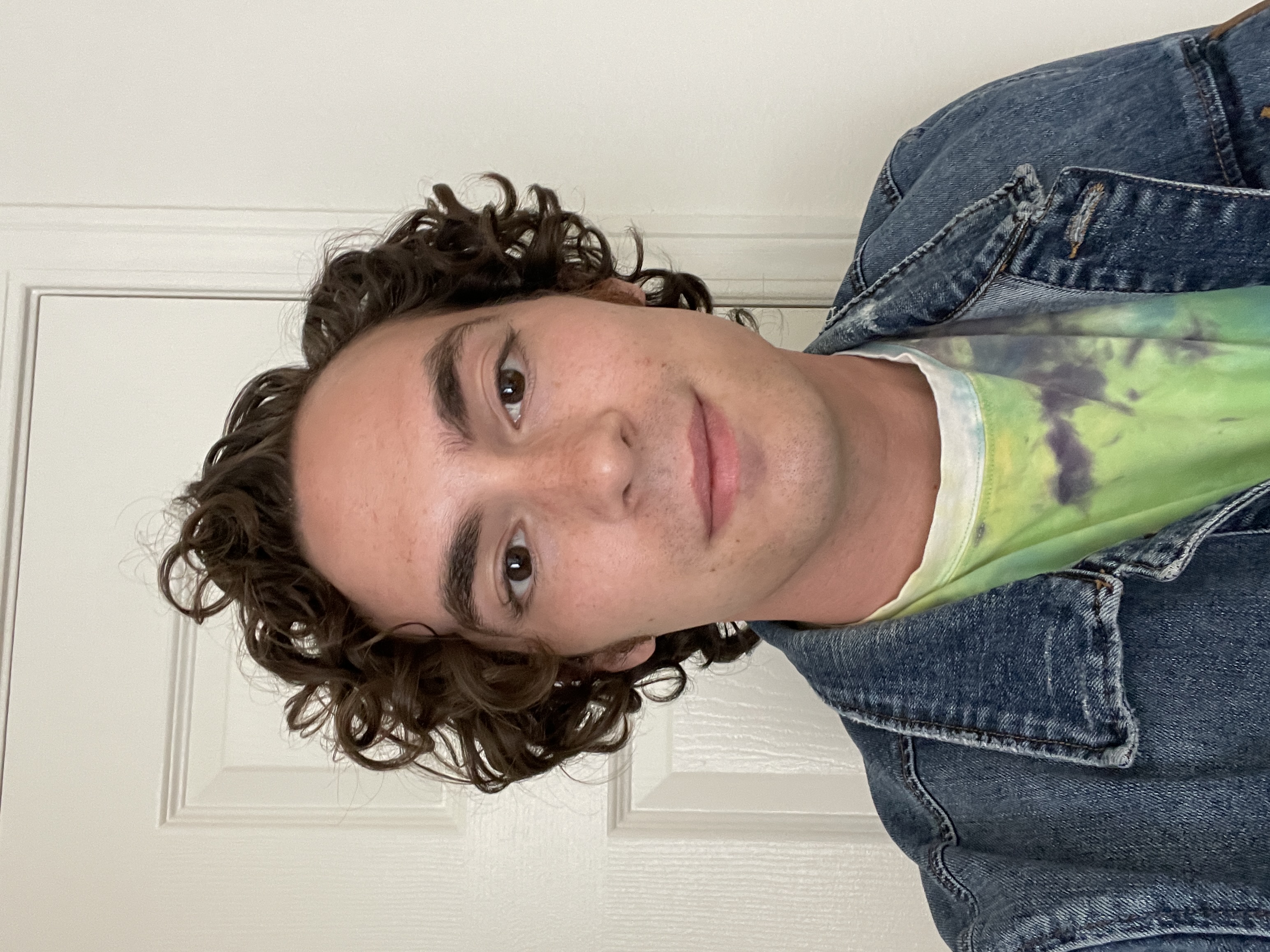 Close-up selfie of Neil in a denim jacket against a plain white door, natural light
