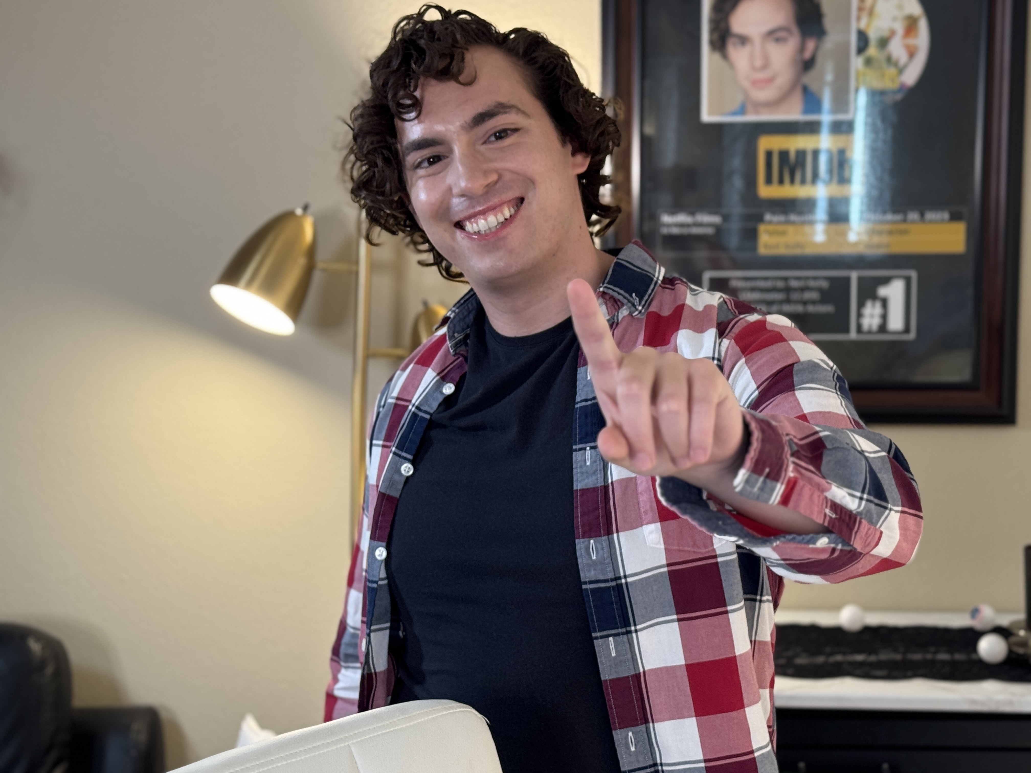 Neil in his home office pointing at the camera, framed IMDb listing on the wall behind him